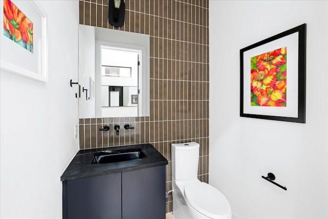 half bath featuring toilet, tile walls, vanity, and decorative backsplash