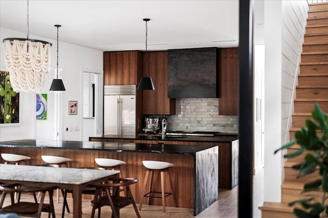 kitchen with an inviting chandelier, modern cabinets, tasteful backsplash, dark countertops, and stainless steel built in fridge