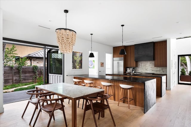 kitchen with tasteful backsplash, wall chimney exhaust hood, modern cabinets, dark countertops, and stainless steel built in refrigerator