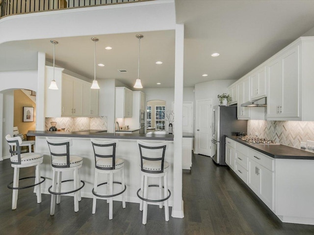 2733 Painted Sky Bnd, Leander, TX 78641 - kitchen featuring under cabinet range hood, dark countertops, stainless steel appliances, decorative backsplash, and white cabinetry