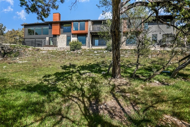 1903 Toro Canyon Rd, Austin, TX 78746 - rear view of house featuring a chimney, stone siding, and a lawn