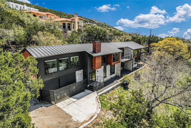 1903 Toro Canyon Rd, Austin, TX 78746 - view of front of home featuring a standing seam roof, stone siding, a chimney, and a metal roof