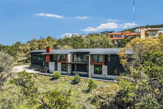 1903 Toro Canyon Rd, Austin, TX 78746 - back of house featuring stone siding, a standing seam roof, a chimney, and a metal roof