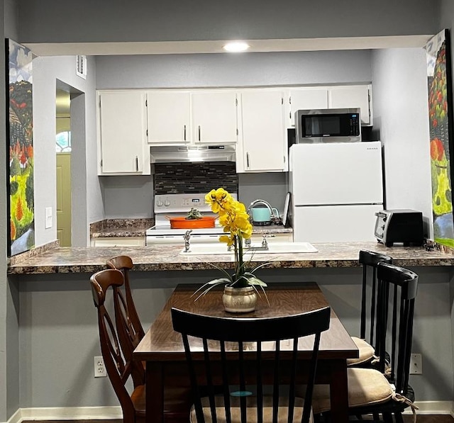 kitchen featuring white cabinets, a kitchen breakfast bar, white appliances, a peninsula, and under cabinet range hood