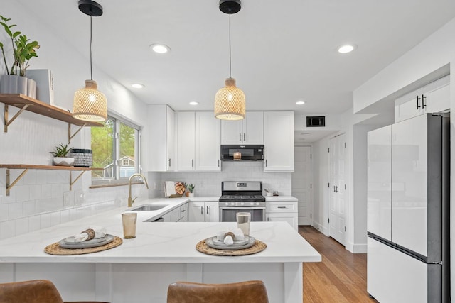 kitchen featuring stainless steel gas range, freestanding refrigerator, black microwave, a sink, and open shelves
