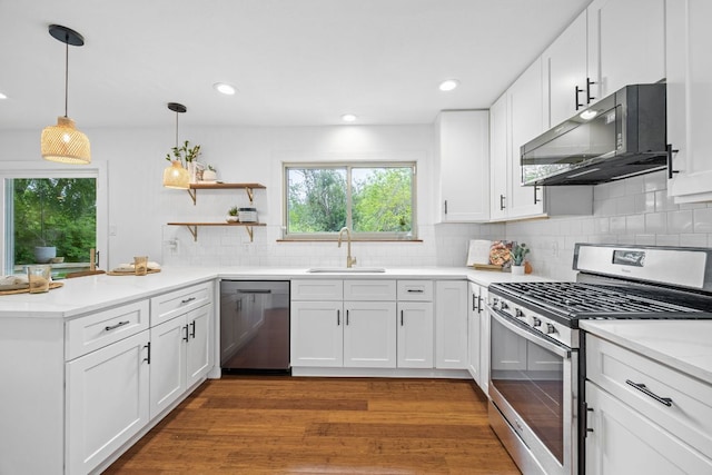kitchen with appliances with stainless steel finishes, a sink, a peninsula, wood finished floors, and white cabinetry