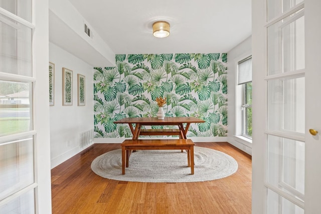 dining room featuring wallpapered walls, an accent wall, baseboards, and wood finished floors