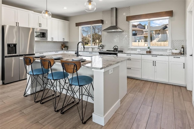 315 Southwind Rd, Point Venture, TX 78645 - kitchen featuring appliances with stainless steel finishes, wall chimney range hood, light wood-type flooring, an island with sink, and decorative backsplash