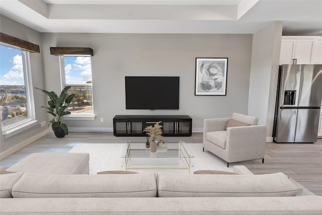 living room featuring baseboards, a tray ceiling, and light wood finished floors