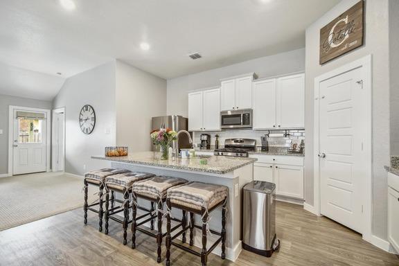 5907 Akin Run, San Antonio, TX 78261 - kitchen featuring appliances with stainless steel finishes, a breakfast bar area, an island with sink, white cabinets, and vaulted ceiling