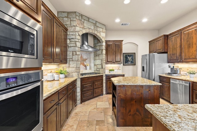201 Aldea St, Georgetown, TX 78633 - kitchen with stainless steel appliances, wall chimney exhaust hood, tasteful backsplash, a kitchen island, and light stone countertops
