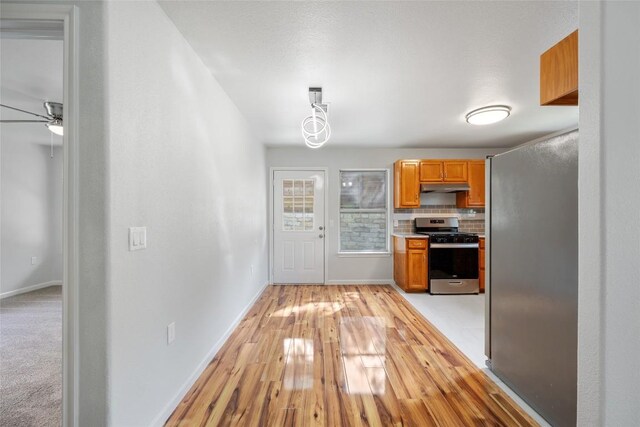 kitchen with under cabinet range hood, tasteful backsplash, a ceiling fan, baseboards, and appliances with stainless steel finishes