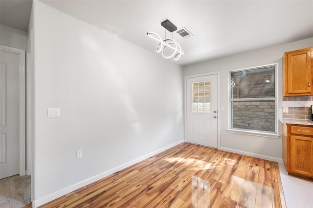 unfurnished dining area featuring baseboards, visible vents, a notable chandelier, and light wood-style floors