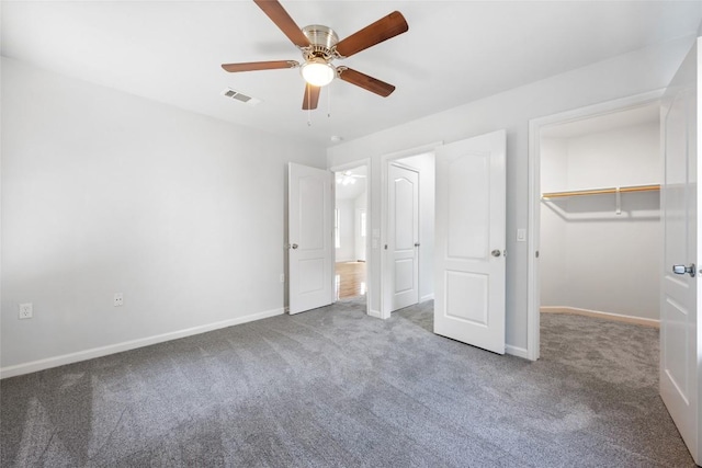 unfurnished bedroom featuring carpet floors, ceiling fan, a walk in closet, baseboards, and visible vents