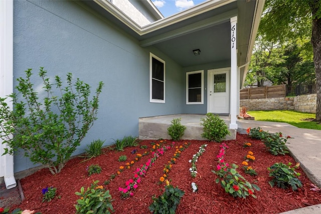 view of exterior entry featuring fence, covered porch, and stucco siding
