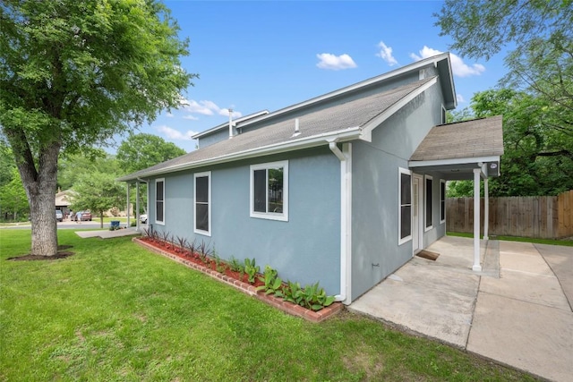 view of property exterior with a patio area, a yard, roof with shingles, stucco siding, and fence