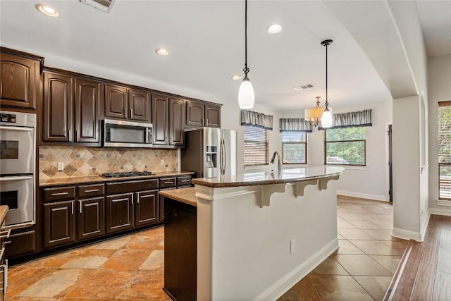 11609 Woodland Hills Trl, Austin, TX 78732 - kitchen with appliances with stainless steel finishes, a kitchen breakfast bar, decorative backsplash, an island with sink, and baseboards