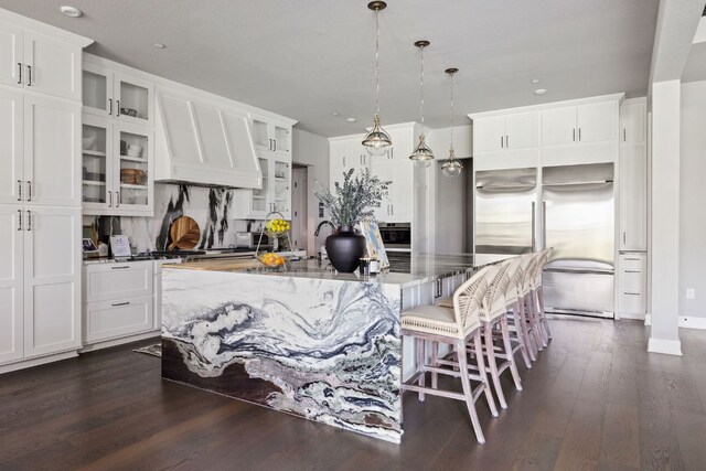 4525 Via Roma Pass, Leander, TX 78641 - kitchen featuring stainless steel built in fridge, dark wood-style flooring, a kitchen island with sink, white cabinetry, and glass insert cabinets