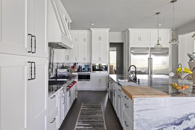 4525 Via Roma Pass, Leander, TX 78641 - kitchen featuring custom range hood, appliances with stainless steel finishes, white cabinets, a kitchen island with sink, and light stone countertops