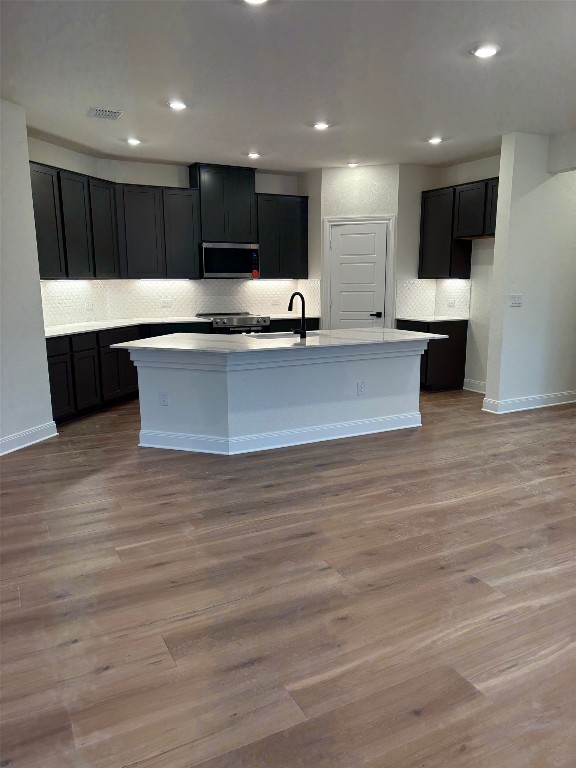 12002 Salvador St, Austin, TX 78748 - kitchen featuring appliances with stainless steel finishes, backsplash, an island with sink, light countertops, and wood finished floors