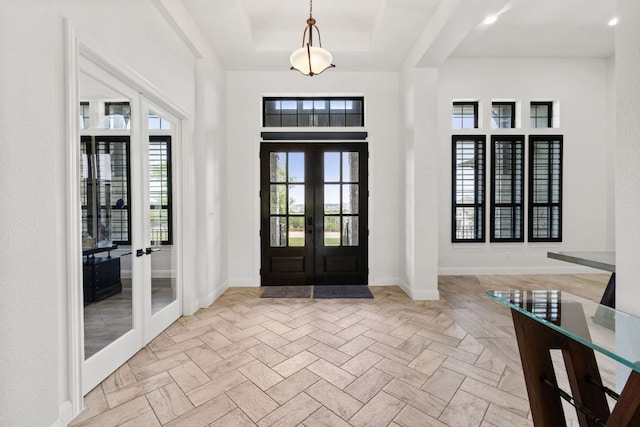 foyer entrance featuring french doors, baseboards, a raised ceiling, and a towering ceiling