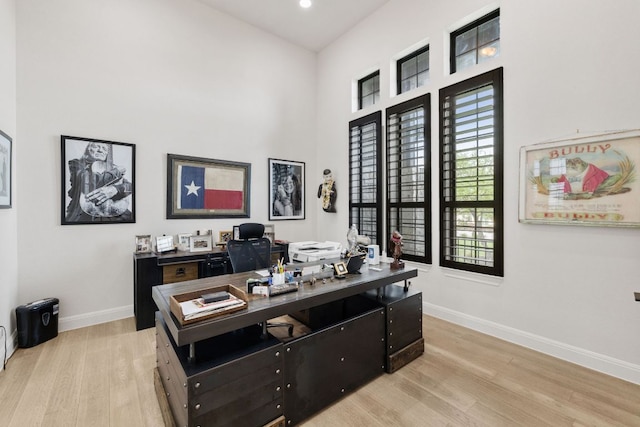 office space with baseboards, a high ceiling, and light wood-style floors