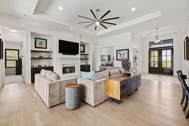 living area with a tray ceiling, a ceiling fan, a glass covered fireplace, and light wood finished floors