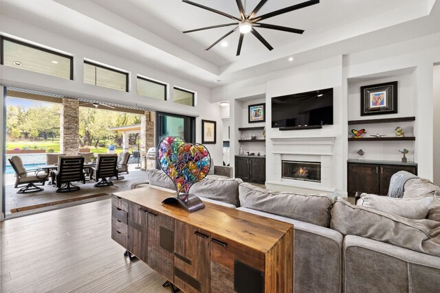17301 Avion Dr, Dripping Springs, TX 78620 - living room featuring a raised ceiling, wood finished floors, recessed lighting, a glass covered fireplace, and a ceiling fan