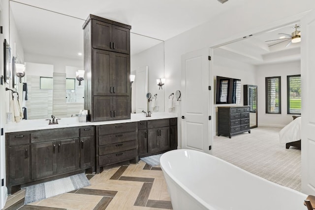bathroom with a raised ceiling, a freestanding bath, double vanity, and a sink