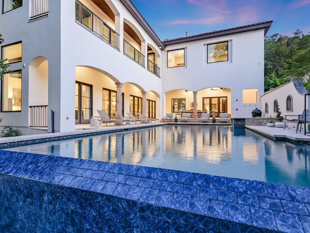 1614 Bruton Springs Rd, Austin, TX 78733 - back of property at dusk with stucco siding, a patio area, an outdoor pool, and a balcony