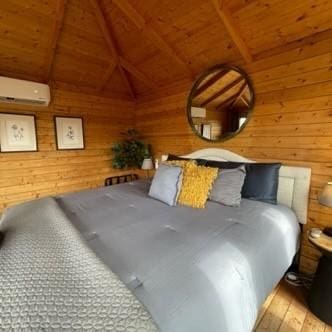 bedroom with wooden ceiling, wood walls, lofted ceiling with beams, and a wall mounted AC