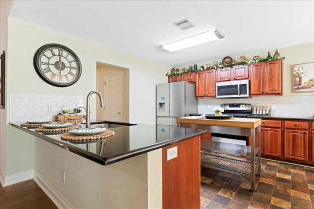 125 Fairway Ct, Bastrop, TX 78602 - kitchen featuring stainless steel appliances, dark countertops, decorative backsplash, a peninsula, and brown cabinetry