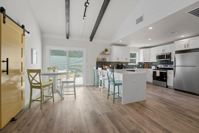 12635 Live Oak Ln, Buda, TX 78610 - kitchen featuring appliances with stainless steel finishes, a barn door, tasteful backsplash, white cabinetry, and beam ceiling