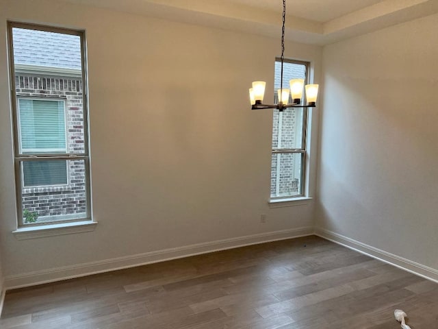 empty room with baseboards, a chandelier, a wealth of natural light, and dark wood-type flooring