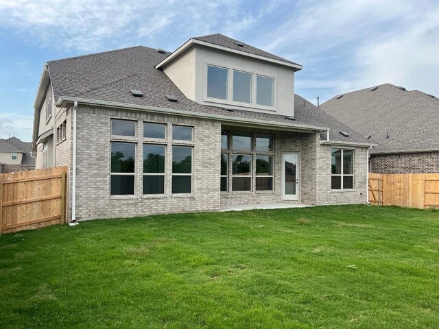 back of property with a fenced backyard, a shingled roof, a yard, and brick siding