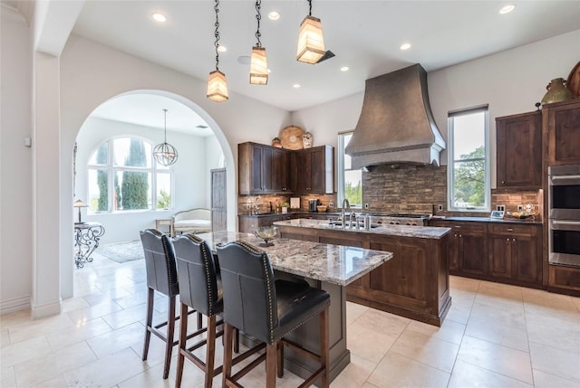 1300 Apache Tears, Horseshoe Bay, TX 78657 - kitchen featuring custom range hood, a kitchen island with sink, backsplash, recessed lighting, and double oven