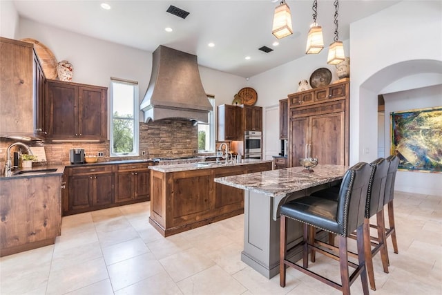 1300 Apache Tears, Horseshoe Bay, TX 78657 - kitchen with premium range hood, an island with sink, tasteful backsplash, recessed lighting, and dark stone countertops