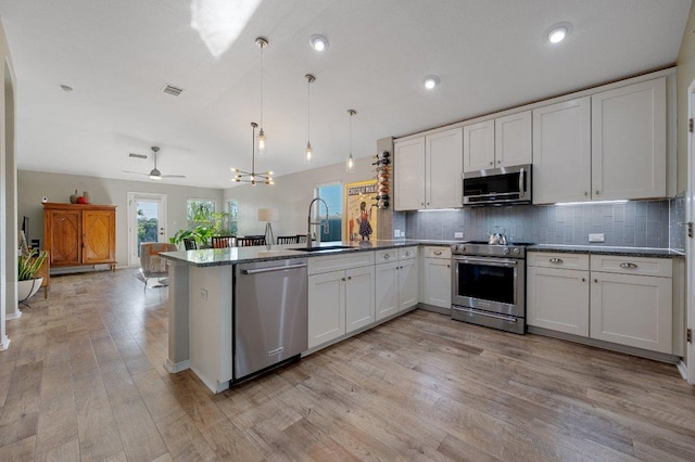 17500 Bridgefarmer Blvd, Pflugerville, TX 78660 - kitchen featuring appliances with stainless steel finishes, a peninsula, decorative backsplash, light wood-style floors, and decorative light fixtures