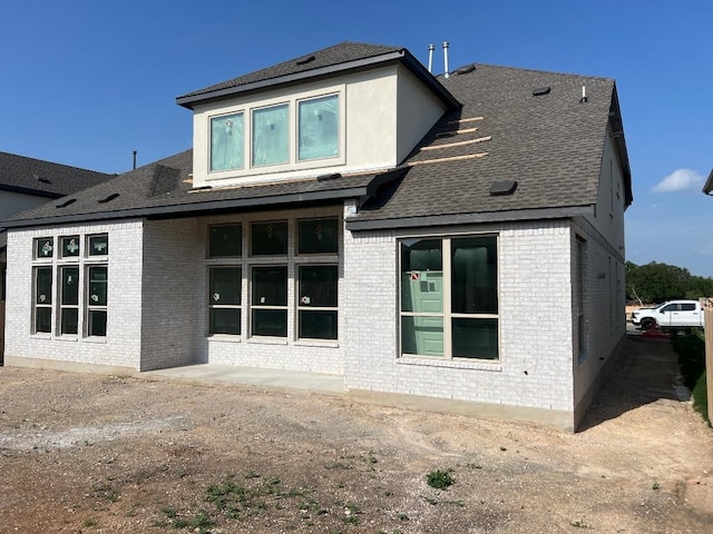 rear view of property featuring brick siding and roof with shingles