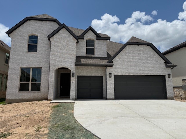 1824 Lazy Grove Bnd, Leander, TX 78641 - french country inspired facade featuring driveway, brick siding, a garage, and roof with shingles