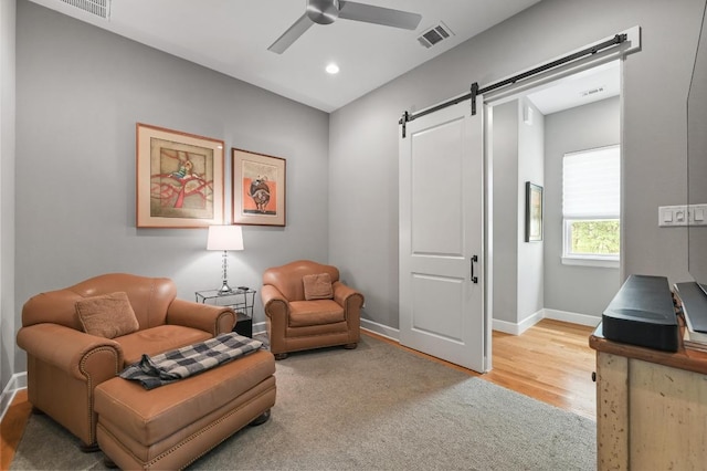 living area with a ceiling fan, visible vents, a barn door, wood finished floors, and baseboards