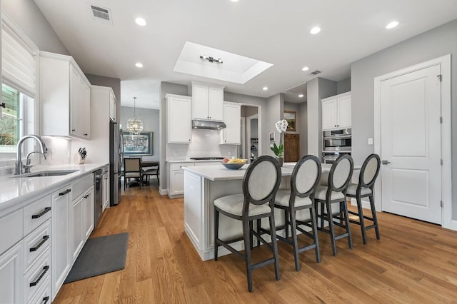 kitchen with a breakfast bar, under cabinet range hood, visible vents, appliances with stainless steel finishes, and a sink