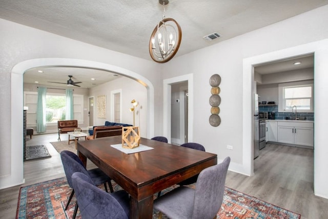 dining room featuring visible vents, light wood-type flooring, arched walkways, and ceiling fan with notable chandelier