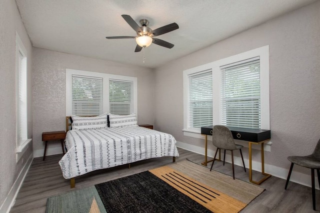 bedroom with a textured wall, ceiling fan, baseboards, and wood finished floors