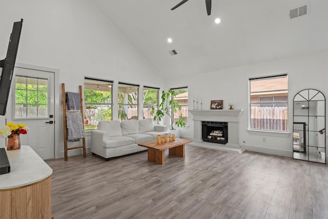 living area with high vaulted ceiling, visible vents, ceiling fan, and wood finished floors