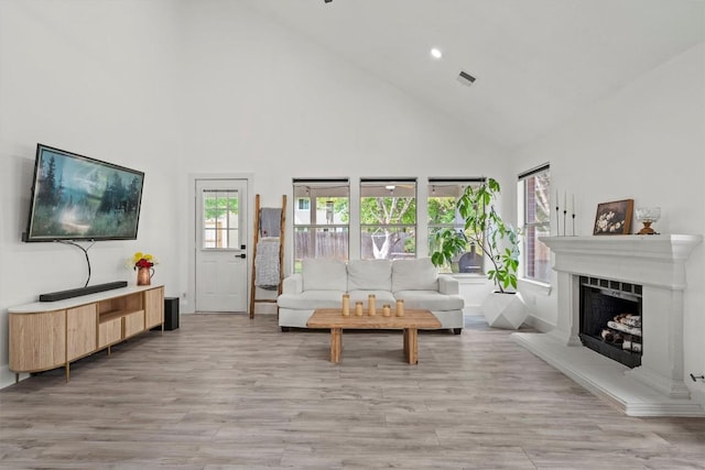 living room with visible vents, a fireplace with raised hearth, light wood finished floors, and high vaulted ceiling