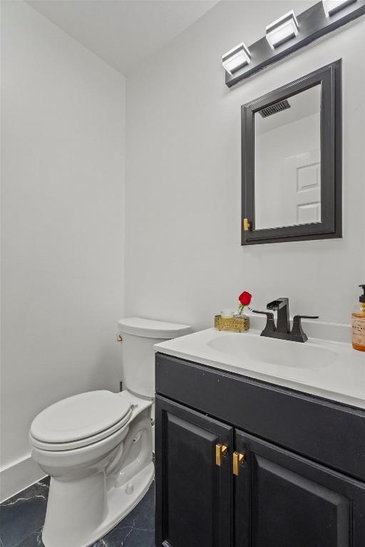 half bath featuring vanity, marble finish floor, visible vents, and toilet