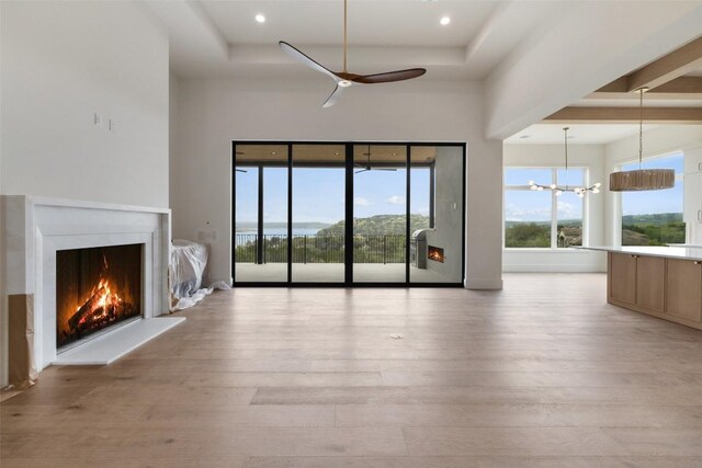 19538 Sandcastle Dr, Spicewood, TX 78669 - unfurnished living room with light wood-style flooring, a raised ceiling, a lit fireplace, and ceiling fan with notable chandelier
