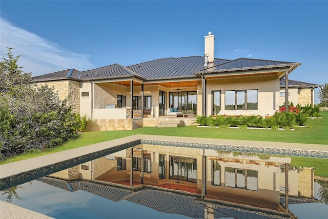 back of house featuring a standing seam roof, a chimney, stucco siding, metal roof, and a yard