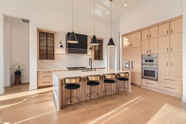 kitchen with a breakfast bar, light countertops, a towering ceiling, wall chimney range hood, and light brown cabinetry